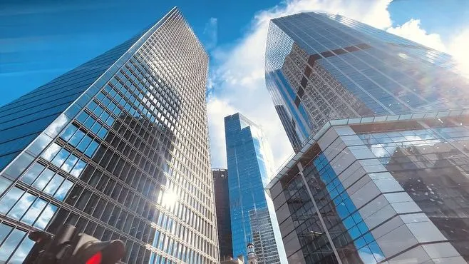 This may contain: some very tall buildings in the city with blue sky and clouds behind them on a sunny day