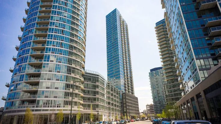 This may contain: some very tall buildings in the city with cars parked on the side of the road