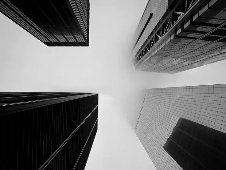 This may contain: black and white photograph of skyscrapers from the ground looking up at one another with sky in background