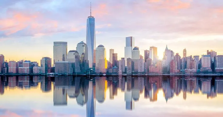 This may contain: the skyline of new york city is reflected in the water at sunset, with skyscrapers and other tall buildings