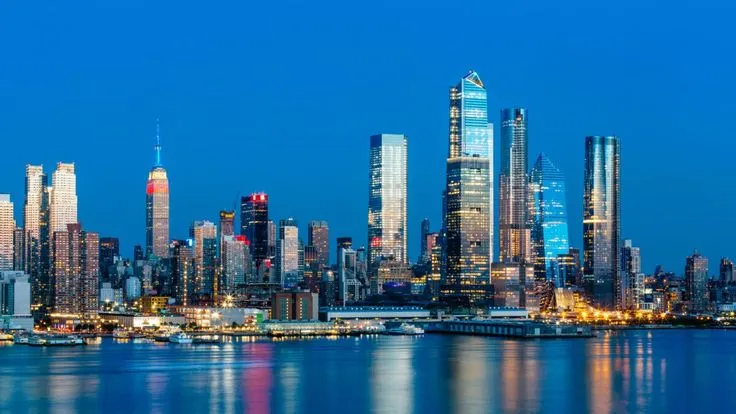This may contain: the city skyline is lit up at night, with bright lights reflecting in the water