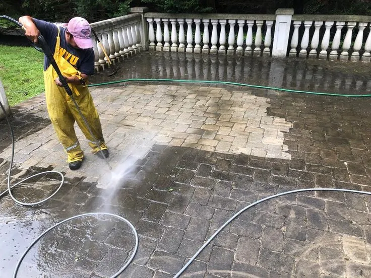 This may contain: a man in yellow overalls is spraying water on a patio with a hose and sprayer