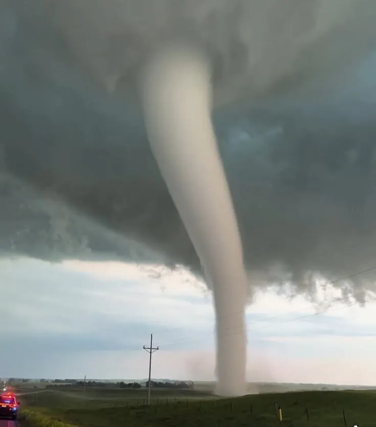 This may contain: a large tornado is seen in the sky over a road