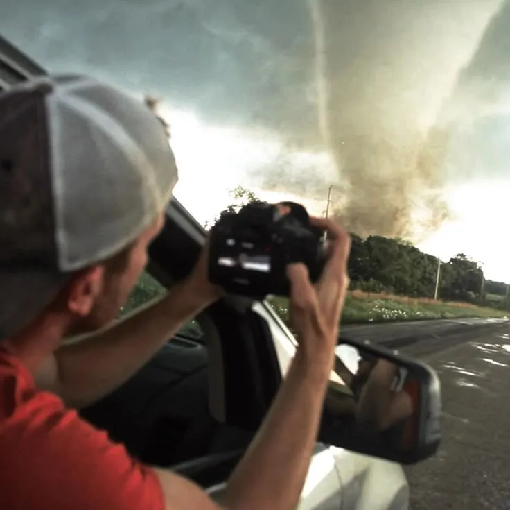 This may contain: a man taking a picture of a large tornado