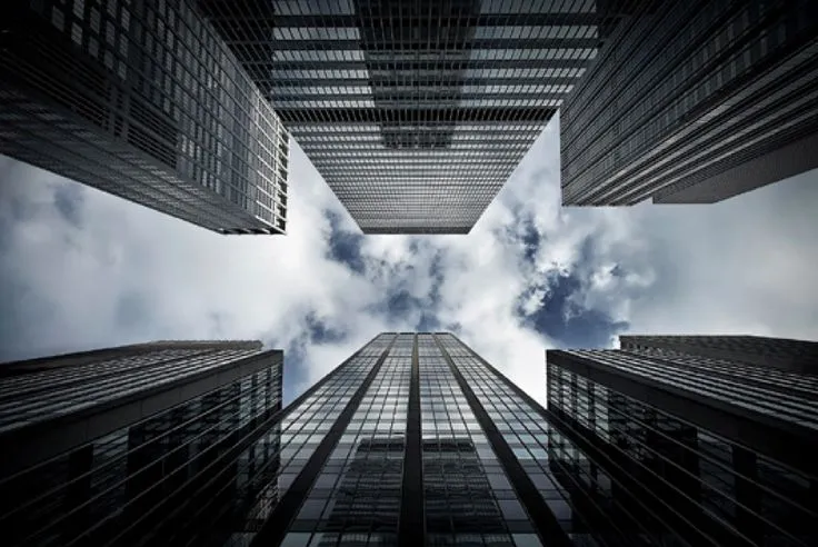 This may contain: looking up at skyscrapers from the ground with clouds and blue sky in the background