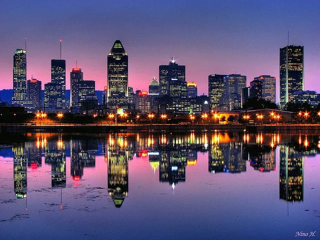 This may contain: the city skyline is lit up at night as seen from across the water with reflections in the water