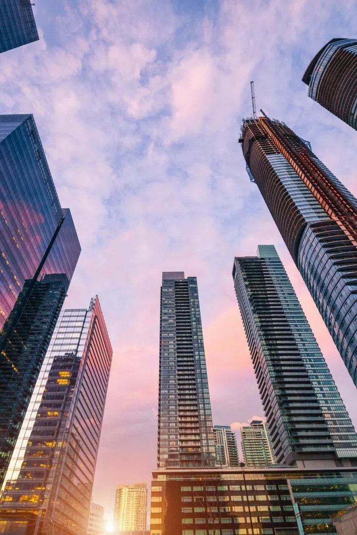 This may contain: tall skyscrapers in the city at sunset with pink and blue sky behind them, viewed from ground level
