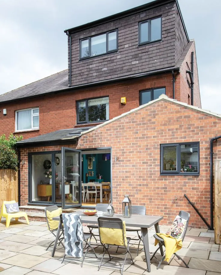 This may contain: a patio area with chairs and tables in front of a brick building that has an extension door