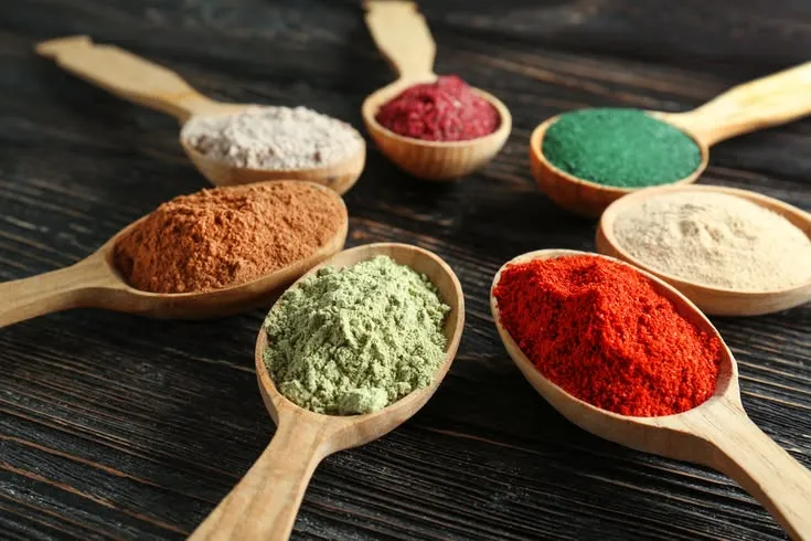 This may contain: five wooden spoons filled with different colored powdered items on top of a table