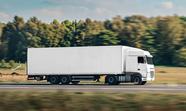 This may contain: a white semi truck driving down the road with trees in the backgrouund