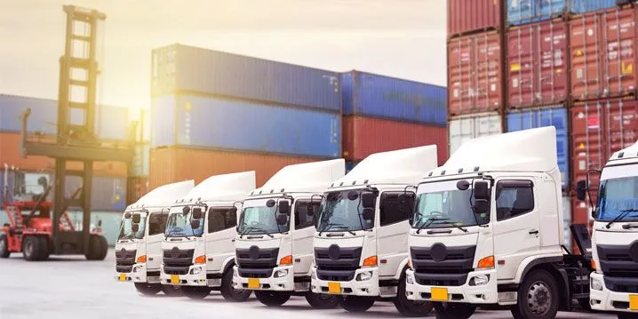 This may contain: a row of white trucks parked next to each other in front of shipping containers on the ground