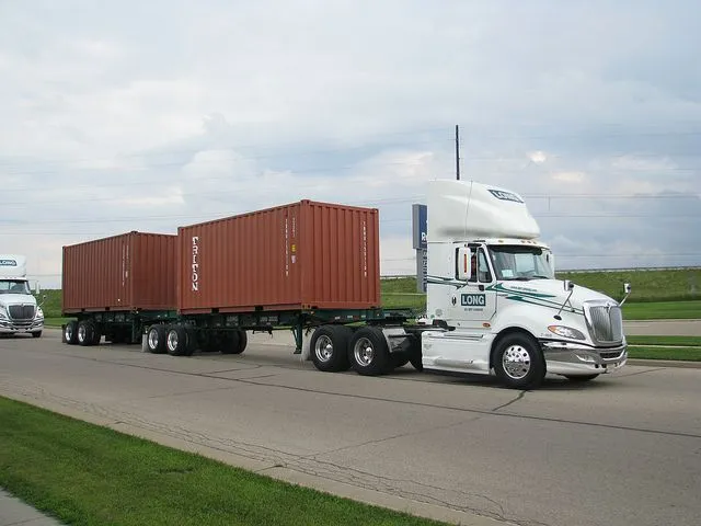 This may contain: two semi trucks driving down the road with cargo containers on their flatbeds behind them