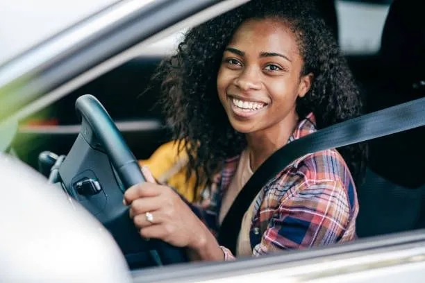 This may contain: a woman sitting in the driver's seat of a car smiling at the camera