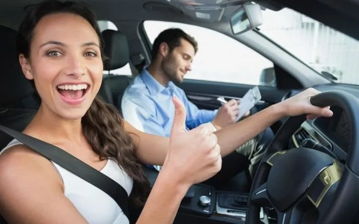 This may contain: a man and woman sitting in the driver's seat of a car giving thumbs up