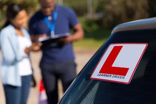 This may contain: a man and woman standing next to a car with a sign on the window that says learn driver