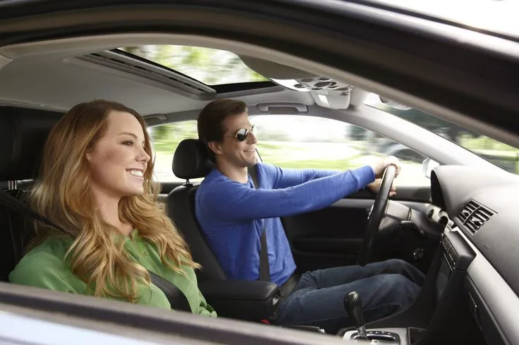 This may contain: a man and woman sitting in the driver's seat of a car, both smiling