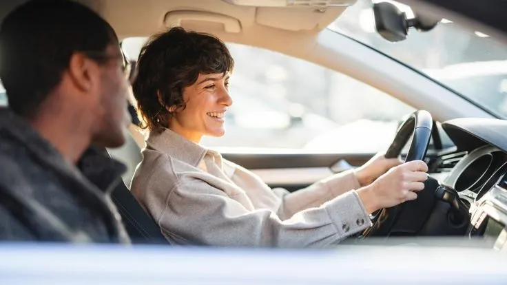 This may contain: a man driving a car with a woman sitting behind the steering wheel and smiling at him