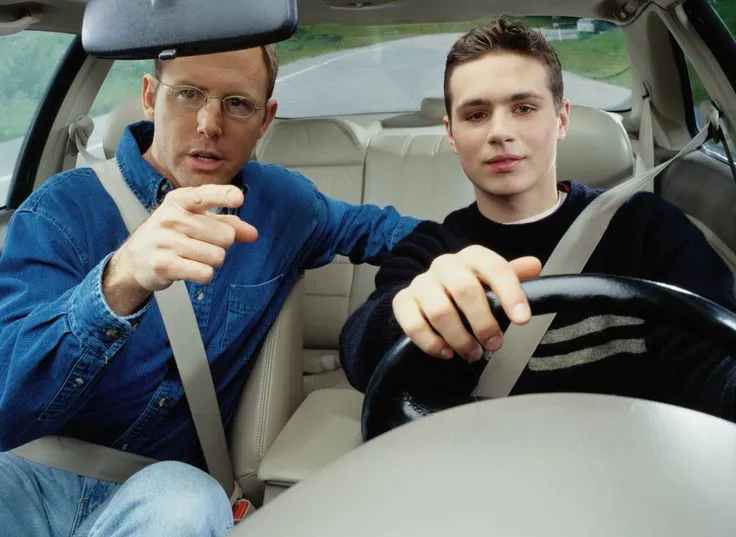 This may contain: two men sitting in the back seat of a car, one pointing at the camera