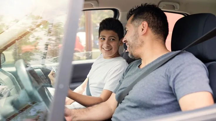 This may contain: a man and boy are sitting in the back seat of a car looking at each other