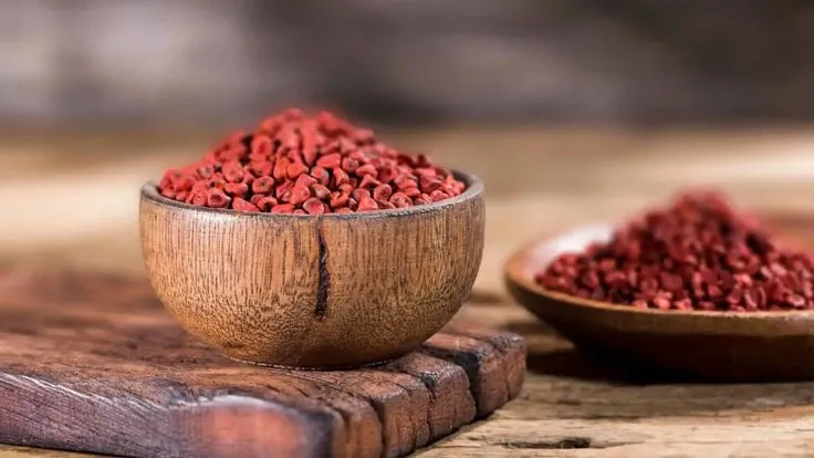 This may contain: a wooden bowl filled with red food next to a spoon