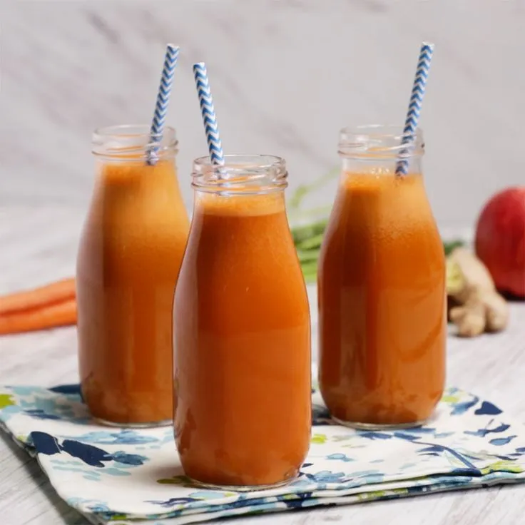 This may contain: three jars filled with orange juice sitting on top of a table next to carrots