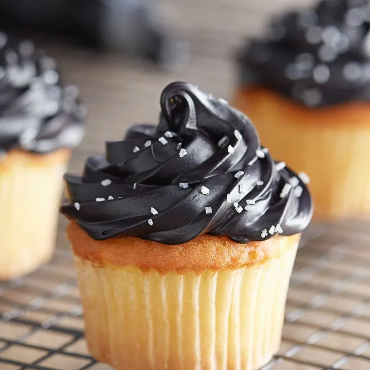 This may contain: cupcakes with black frosting and sprinkles on a cooling rack