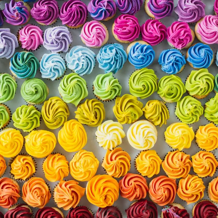 This may contain: cupcakes with different colored frosting are arranged in rows