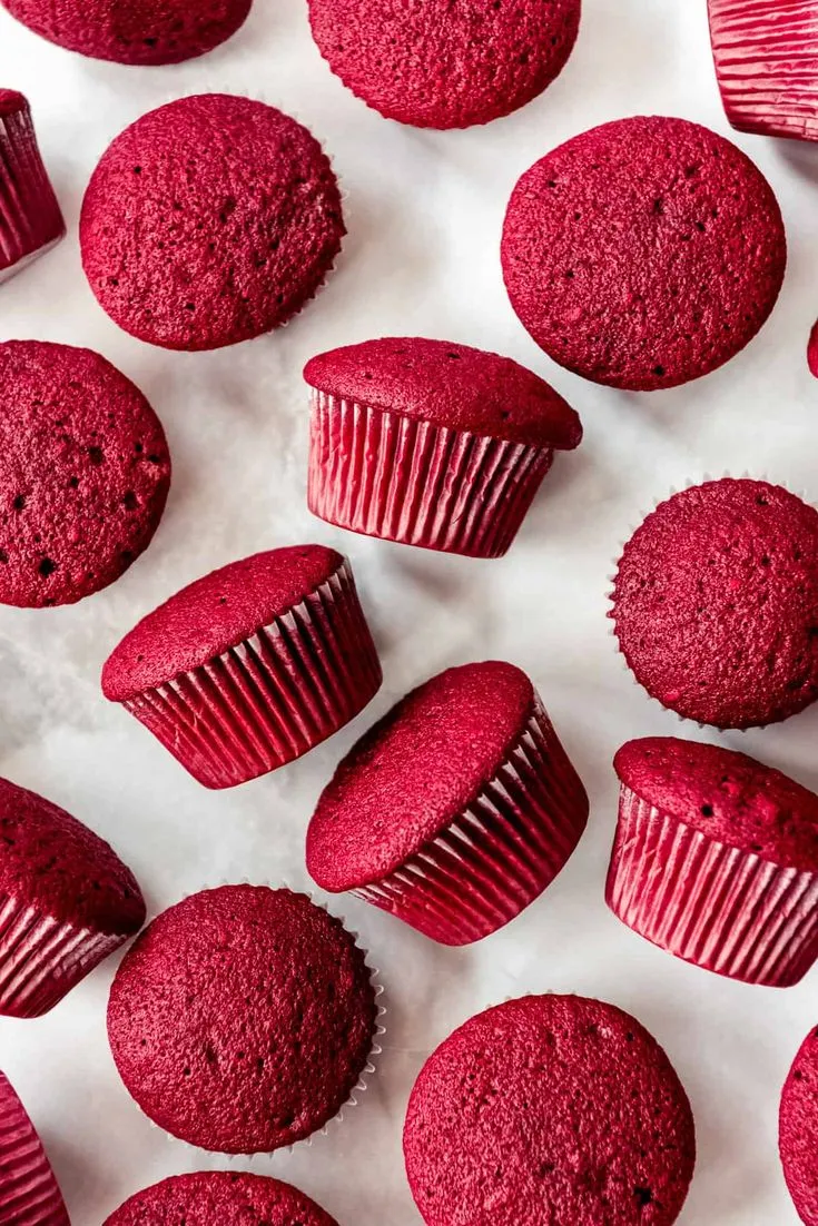 This may contain: red cupcakes and muffins on a white surface with pink frosting