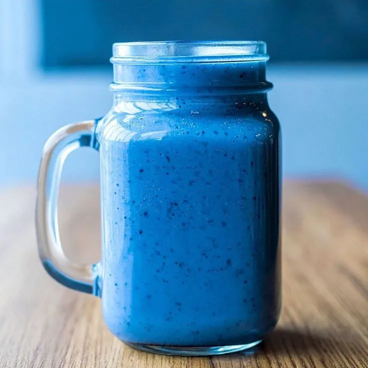 This may contain: a blue drink in a mason jar on a wooden table