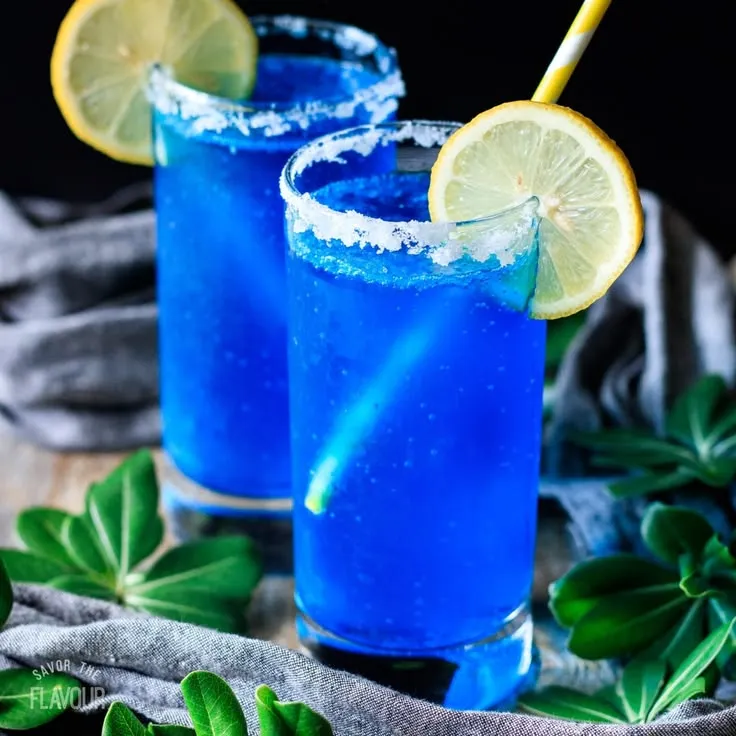 This may contain: two blue cocktails with lemon and sugar garnish