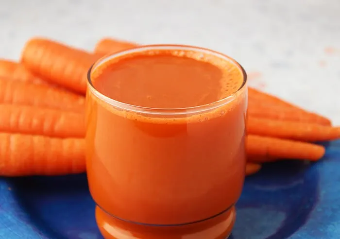 This may contain: carrot juice in a glass on a blue plate
