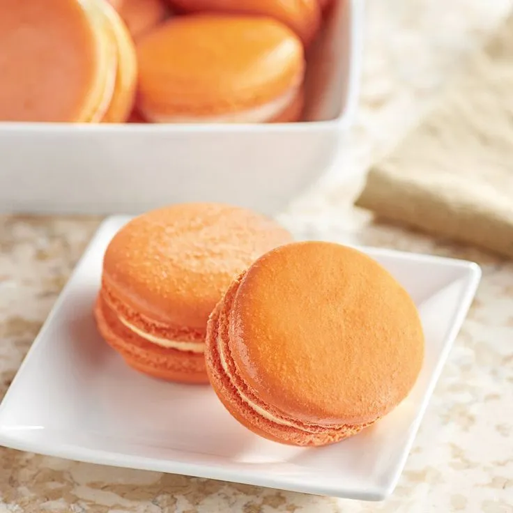 This may contain: two white plates filled with orange macaroons on a table