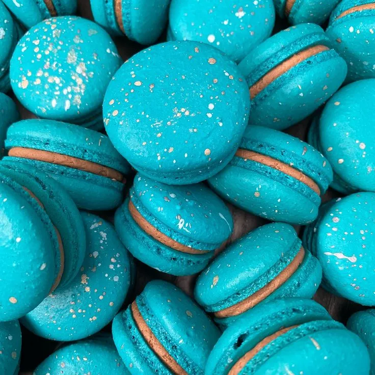 This may contain: blue macaroons with gold sprinkles are piled on top of each other