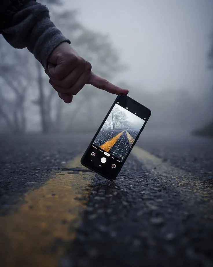 This may contain: a person pointing at an image on their cell phone in the middle of the road