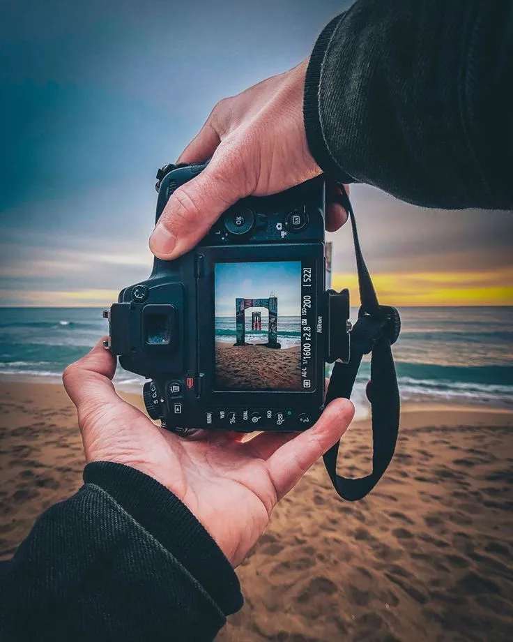 This may contain: a person holding up a camera on the beach