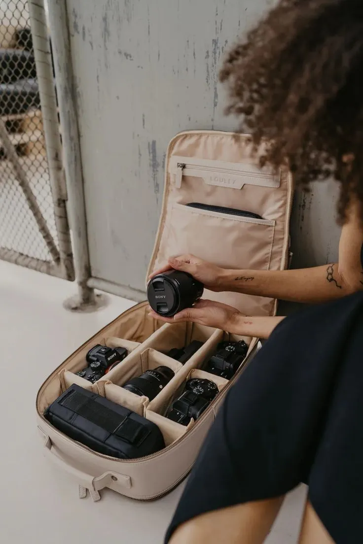 This may contain: a woman sitting in front of an open suitcase filled with camera equipment and looking at it