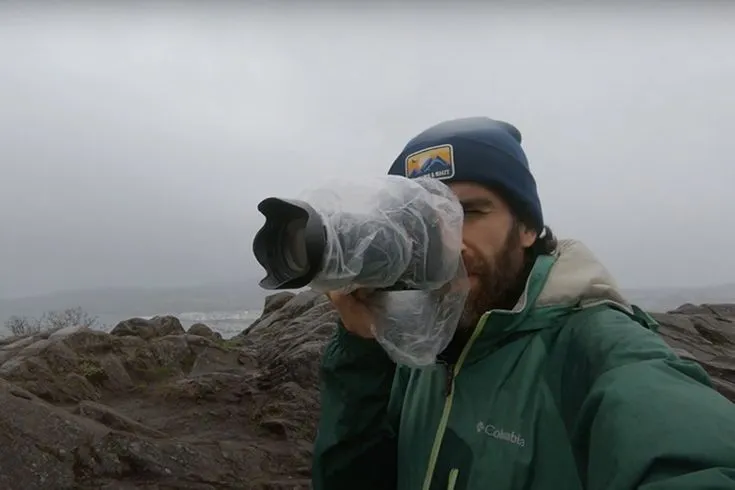 This may contain: a man in a green jacket taking a photo with a camera on top of some rocks