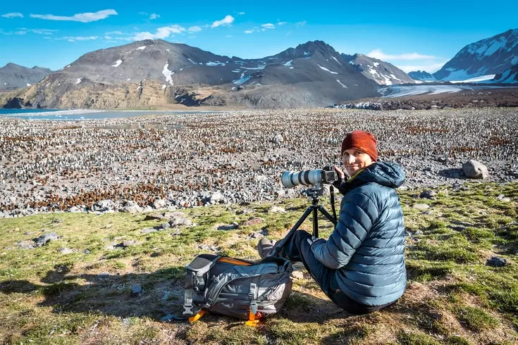 This may contain: a person sitting on the ground with a camera in front of them and mountains in the background