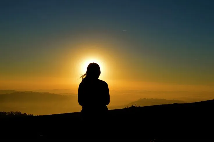 This may contain: a person standing on top of a hill with the sun setting in the sky behind them