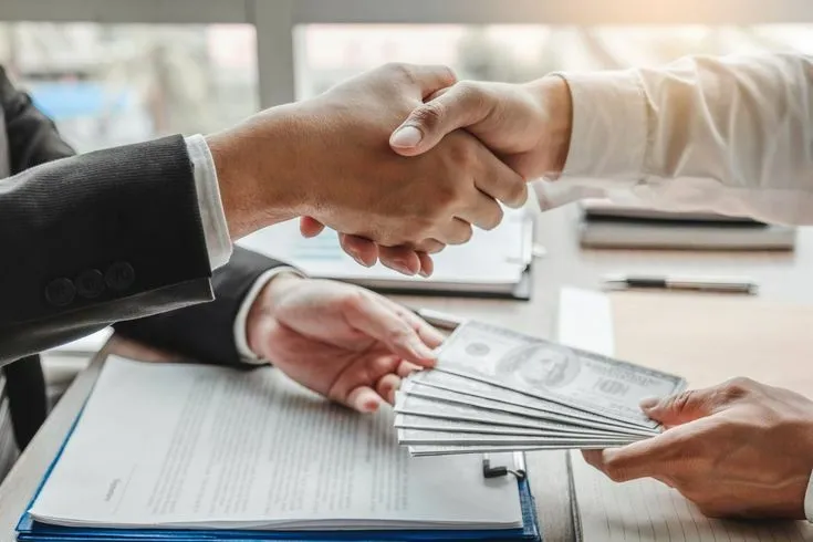 This may contain: two people shaking hands over papers on a table