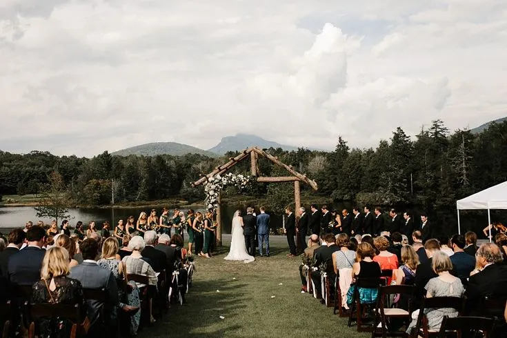 This may contain: an outdoor wedding ceremony with people sitting at the end of the aisle, and mountains in the background