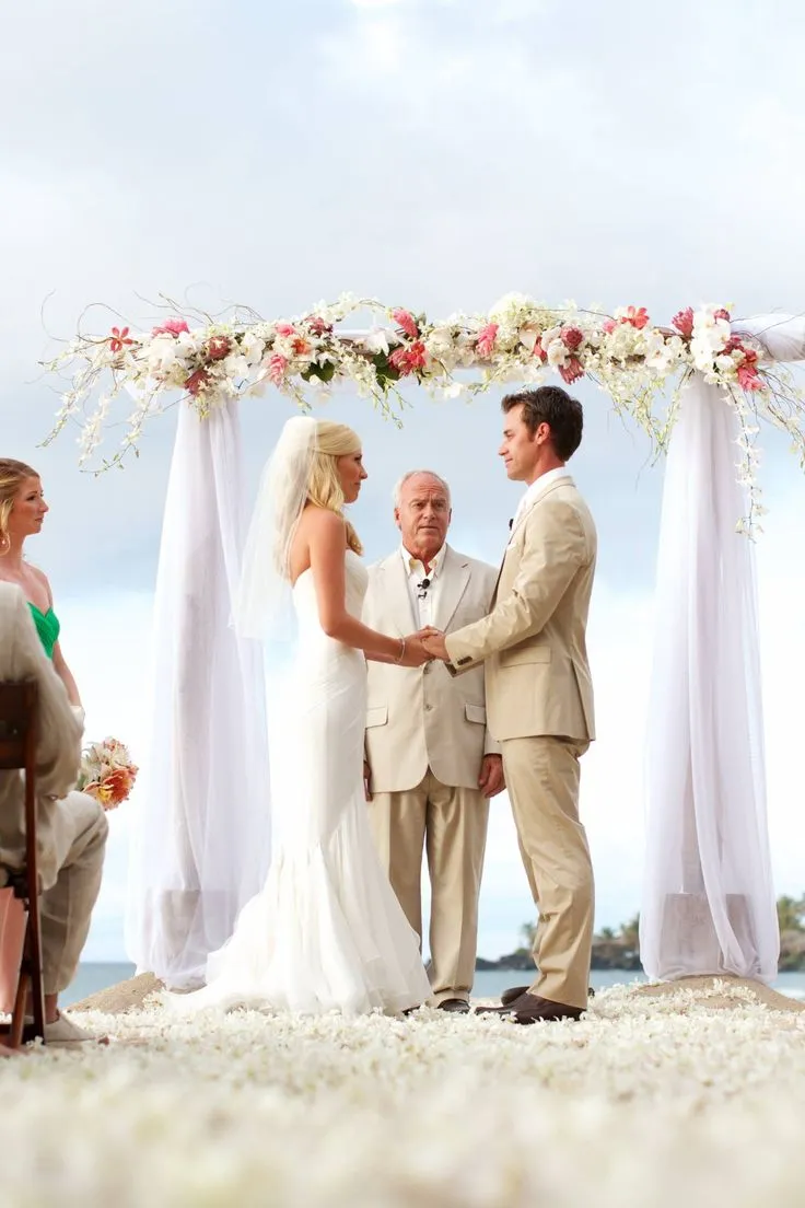 This may contain: a bride and groom standing under an arch with flowers on it at the end of their wedding ceremony