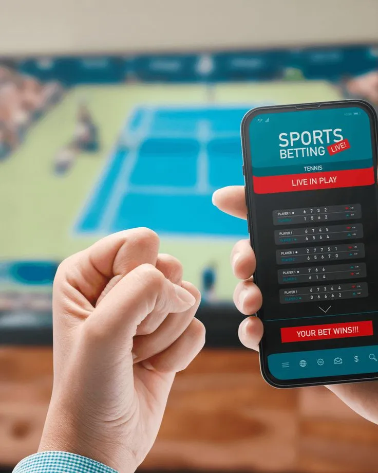 This may contain: a person holding a cell phone in front of a tv with sports betting on it
