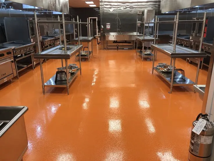 This may contain: an industrial kitchen with orange flooring and stainless steel appliances in the center, surrounded by cabinets