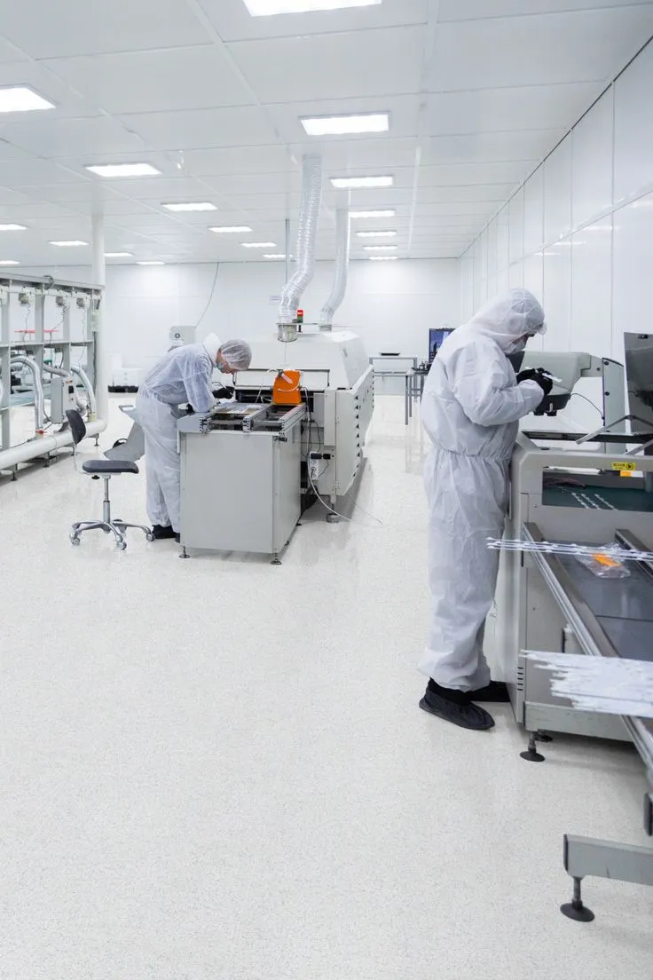 This may contain: two workers in protective clothing are working on machinery inside a factory with white walls and ceilings