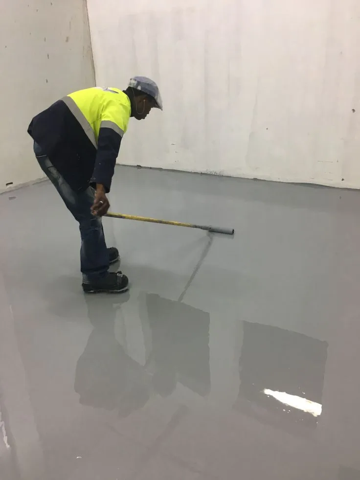 This may contain: a man in yellow shirt and black pants using a broom to clean an industrial floor