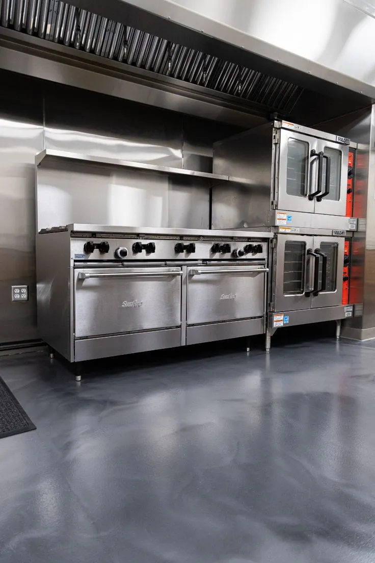 This may contain: an industrial kitchen with stainless steel appliances in it's center and two ovens on each side