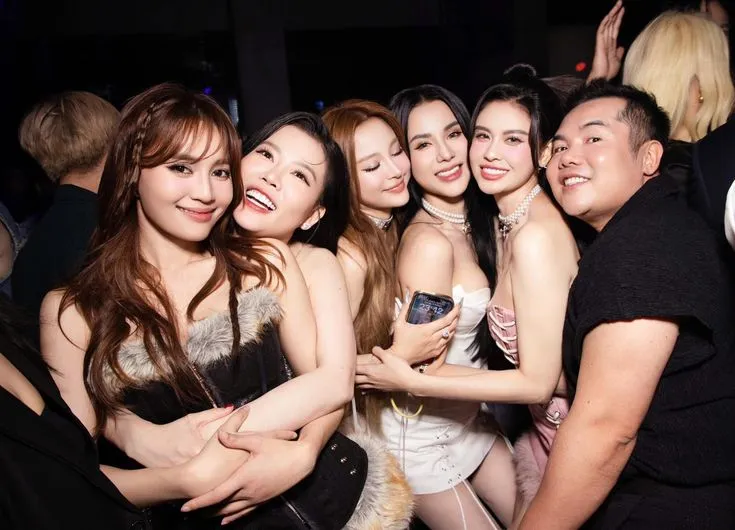 This may contain: a group of women standing next to each other in front of a man holding a cell phone