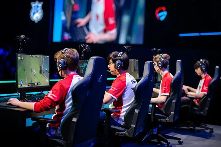 This may contain: four people wearing headphones are playing video games on their computer screens in front of a large screen