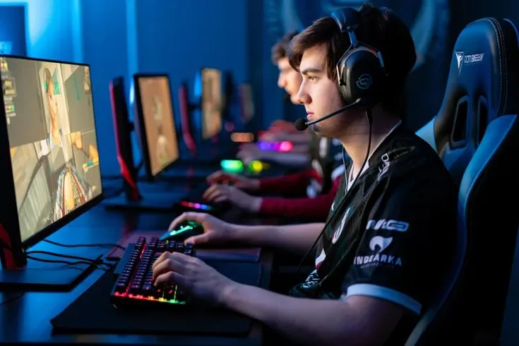 This may contain: two men sitting in front of computer monitors wearing headphones and playing games on their computers